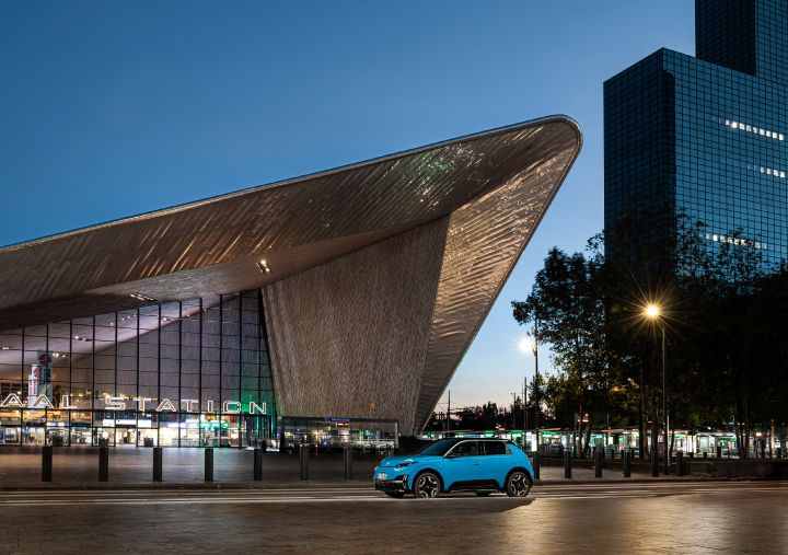 Seitenansicht eines blauen Nissan Micra, der im Abendlicht vor der auffälligen Architektur des Hauptbahnhofs Rotterdam steht