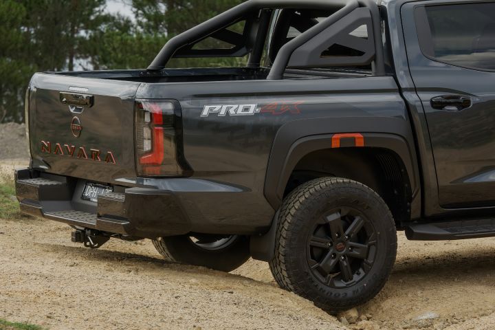 2026 Nissan Navara PRO-4X finished in Boulder Grey focusing on the rear quarter with PRO‑4X bedside graphic, tail‑lamp housing, towbar tongue and tub liner edge.