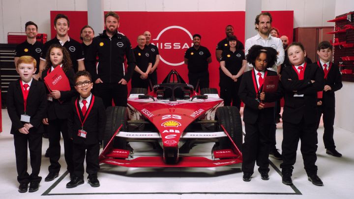 Nissan Formula E team members, and a group of children (the Department of Futures) in black suits standing in front of a red Nissan Formula E race car