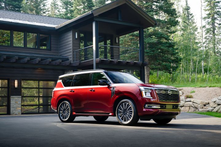 Front right 3/4 view of a red 2025 Nissan Armada parked in front of a large log cabin, trees and brush are behind.