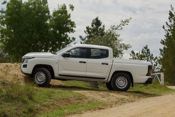2026 Nissan Navara SL dual cab ute finished in Alpine White displayed in full side profile on a dirt incline, highlighting the four-door cabin and utility tray proportions.