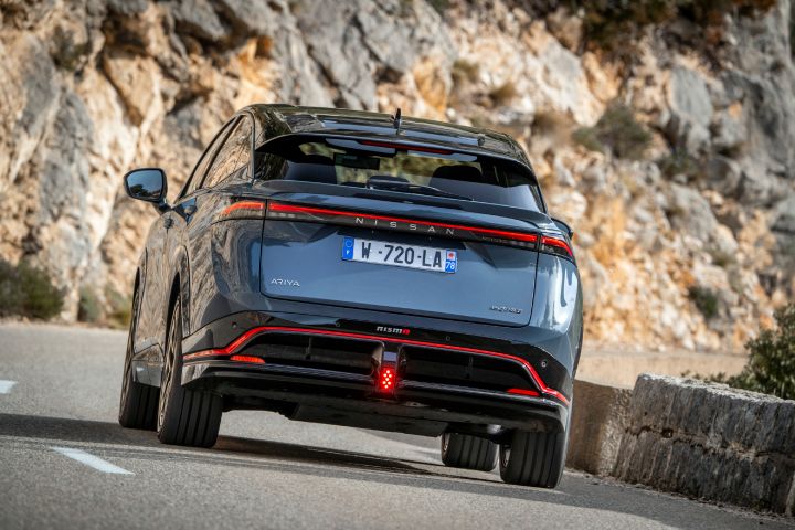 Gros plan sur l’arrière du nouveau Nissan Ariya NISMO roulant aux pieds de la montagne.