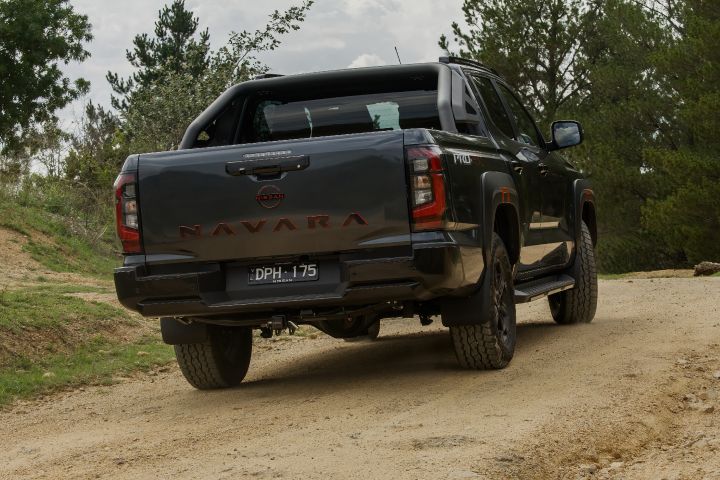 2026 Nissan Navara PRO-4X finished in Boulder Grey positioned front three‑quarter on a grassy knoll with visible wheel droop and red grille inserts.