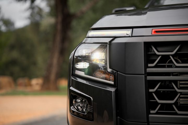 2026 Nissan Navara PRO-4X finished in Boulder Grey showing the illuminated headlight, slim LED strip, black grille pattern and dark front bumper trim.
