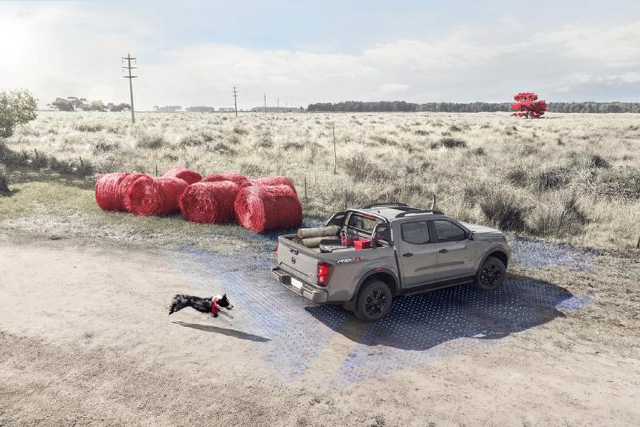 Una Nissan Frontier estacionada en un campo, con un perro que lleva un pañuelo rojo como collar corriendo detrás.