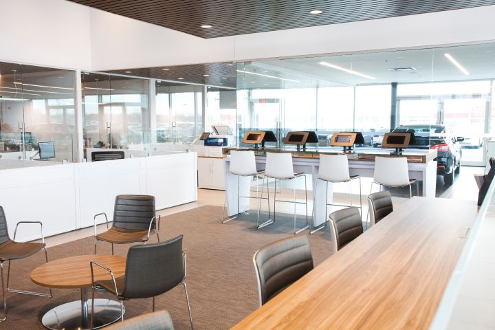 Espace de rédaction moderne avec de hauts tabourets au comptoir, des ordinateurs de bureau sur les bureaux et un coin salon avec des chaises et des tables, doté de grandes fenêtres.