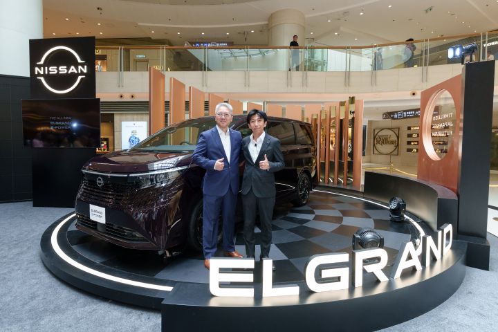 Two people pose beside a Nissan ELGRAND on an auto show display, with a large “ELGRAND” sign and Nissan booth in the background.