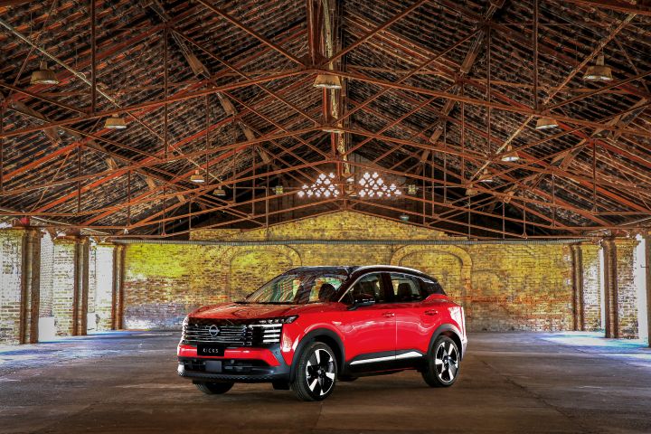 Unidade vemelha com teto preto do Nissan Kicks estacionada em um galpão abandonado e com raios de sol entrando pelas janelas