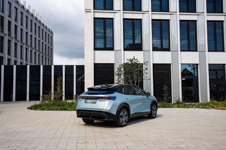 Blick von schräg hinten auf einen hellblauen Nissan Ariya, der vor einem Bürogebäude parkt