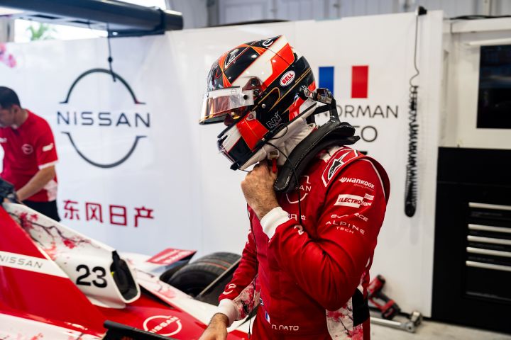 Norman Nato in seinem roten Rennanzug und mit seinem Helm, wie er in der Teamgarage neben seinem Nissan Formel E Rennwagen steht.