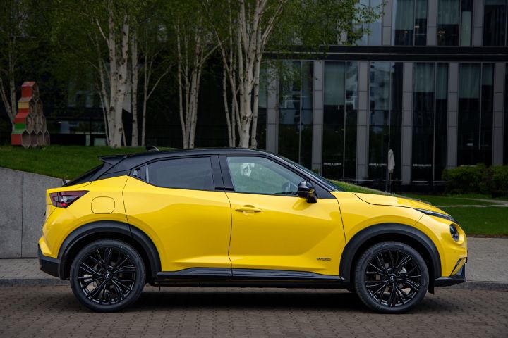 Żółty Nissan Juke stojący bokiem na tle budynku i drzew