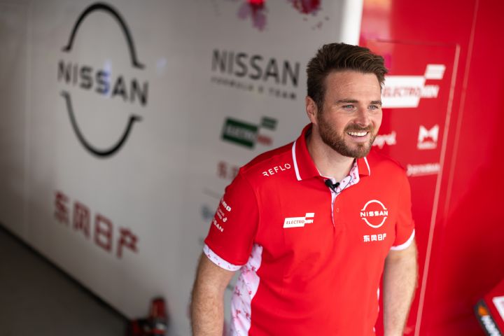 Oliver Rowland in seinem roten Team-Poloshirt lächelt vor der Teamgarage.