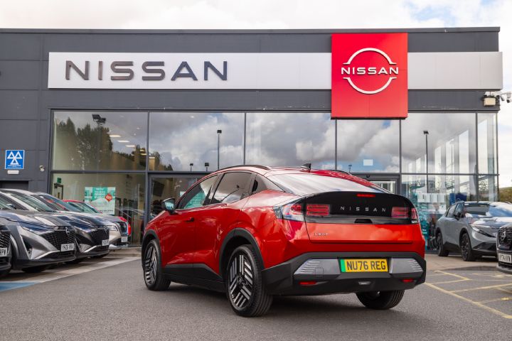 Rear three-quarter view of a red Nissan LEAF parked outside a Nissan dealership