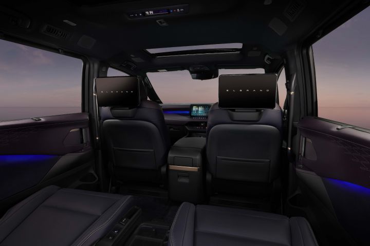 The interior of a Fuji-dawn-colored Elgrand is photographed from the rear seat perspective. The front seat layout and dashboard are visible.