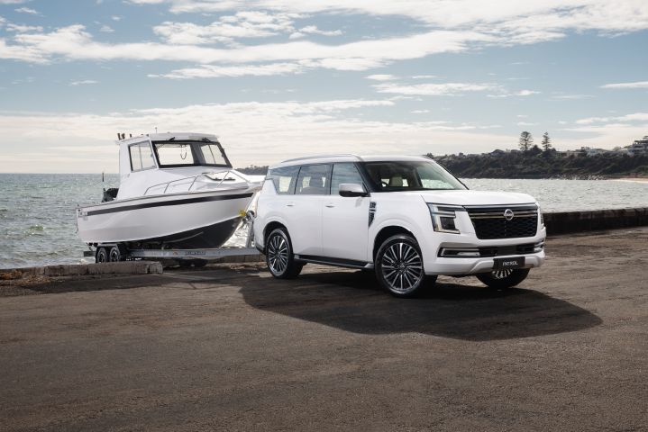 2026 Nissan Y63 Patrol finished in white, shown from a front three-quarter exterior angle on a coastal boat ramp towing a large white boat.