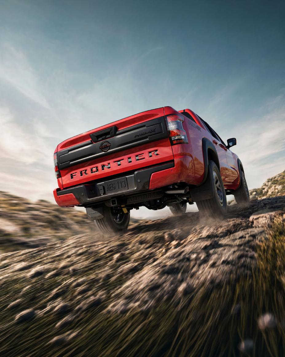 Lower angled rearview of a 2026 Nissan Frontier driving over a dirt path.
