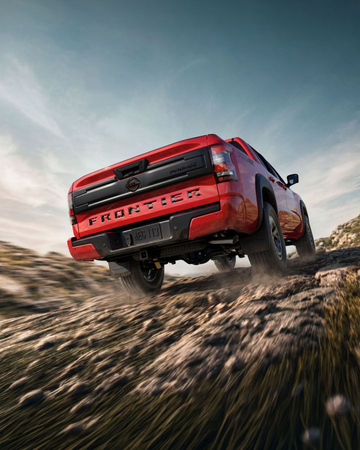 Lower angled rearview of a 2026 Nissan Frontier driving over a dirt path.