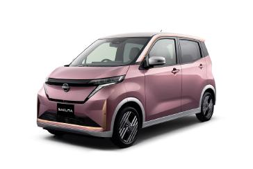 ピンク色の「日産サクラ」を無地の明るい背景で、車両の左前方から斜め前向きに捉えた画像。フロントマスクと側面が強調され、落ち着いたカラーリングが際立っている。