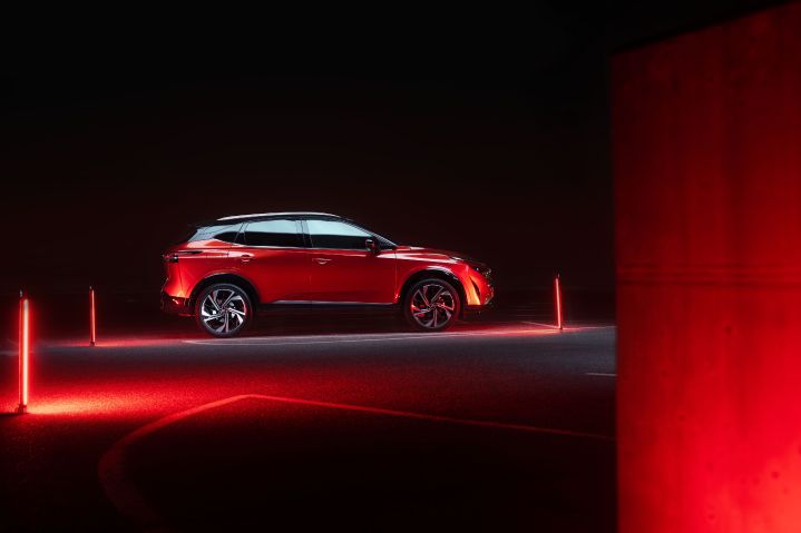 Ein Nissan Qashqai in Fuji Sunset Red steht im Dunkeln seitlich auf einem Parkplatz mit roten Leuchtakzenten vor dem schwarzen Hintergrund