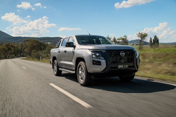 2026 Nissan Navara ST dual cab ute finished in Summit Silver captured from the front-left while driving on a dirt road through bushland.