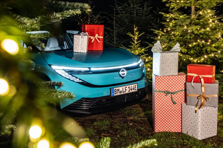 Blick durch Tannenzweige auf einen türkisblauen Nissan LEAF und viele verpackte Weihnachtsgeschenke