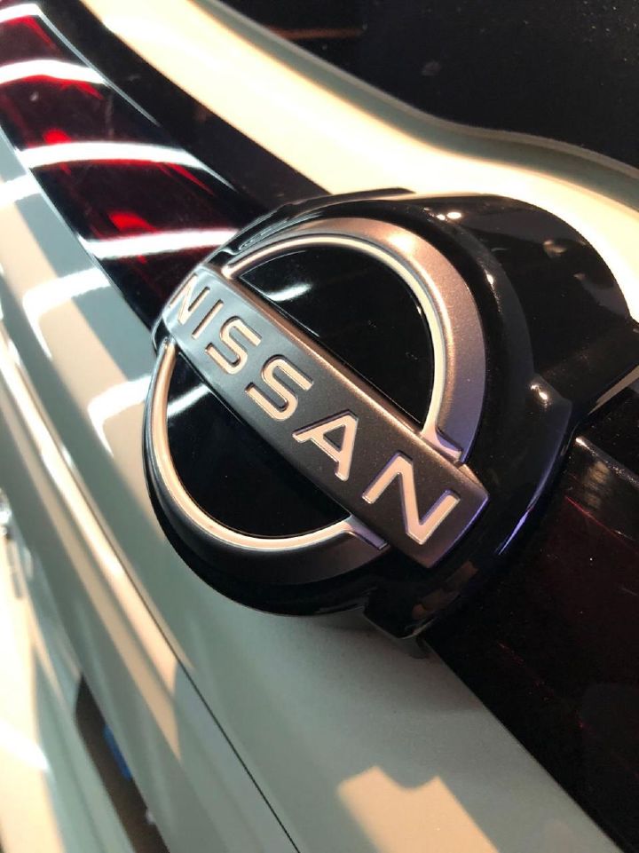 Close-up do logotipo cromado da Nissan sobre fundo preto e branco na traseira de um veículo