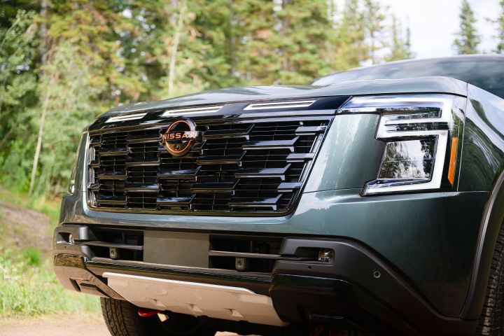 Angled close up of the front end, black grill and centered red Nissan logo on a 2025 Nissan Armada Pro 4X,