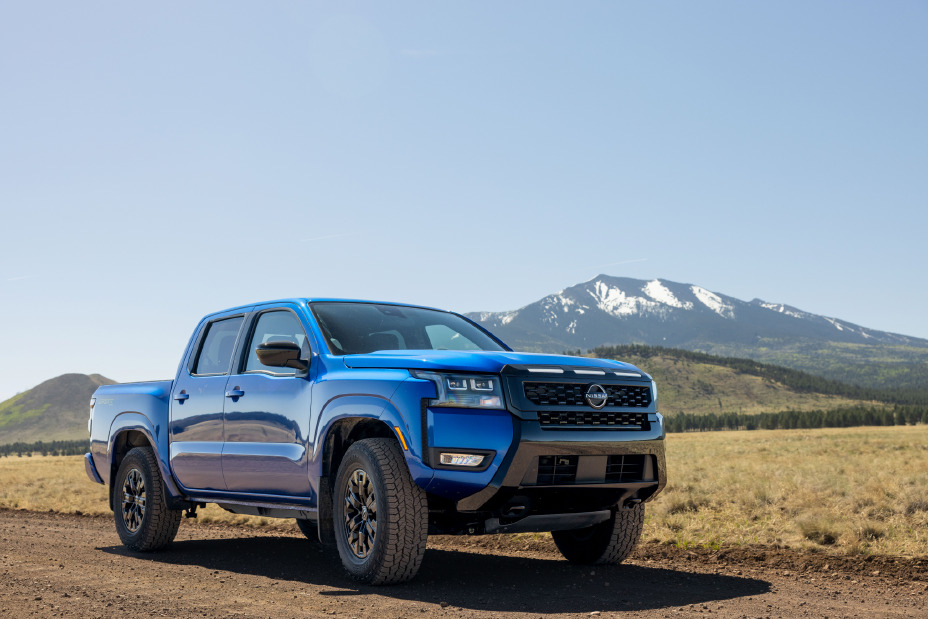 Front right 3/4 view of the 2027 Nissan Frontier Sport Edition parked on a dirt road with mountains behind.
