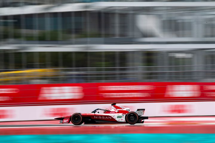 Dynamische Seitenansicht von Norman Nato, der beim Miami E-Prix mit seinem Nissan Formula E Rennwagen an verschwommen zu sehenden rot-weißen Werbebannern vorbeifährt