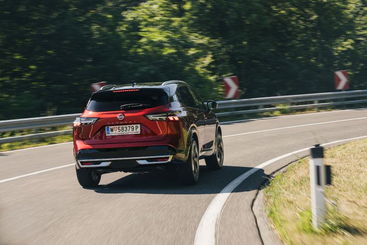 Heck-Fahraufnahme eines Nissan Qashqai in Fuji Sunset Red auf einer kurvigen Landstraße