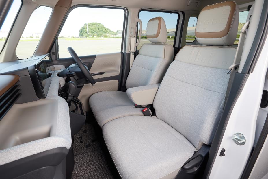 Interior of the new Nissan Roox kei car, showing the greige driver's and passenger seats with headrests. The outside scenery is visible through the windows.
