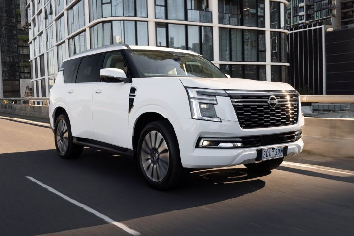 2026 Nissan Y63 Patrol finished in white rolling front 3/4 exterior image driving on an urban road with modern high-rise buildings in the background