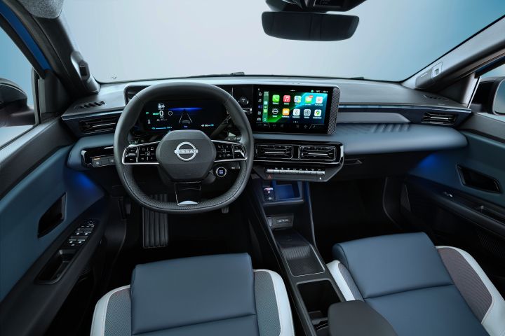 Driver pov of full dashboard cockpit showing steering wheel, driver focused infotainment, rear view mirror, blue ambient lighting below dashboard, front seats and side mirrors