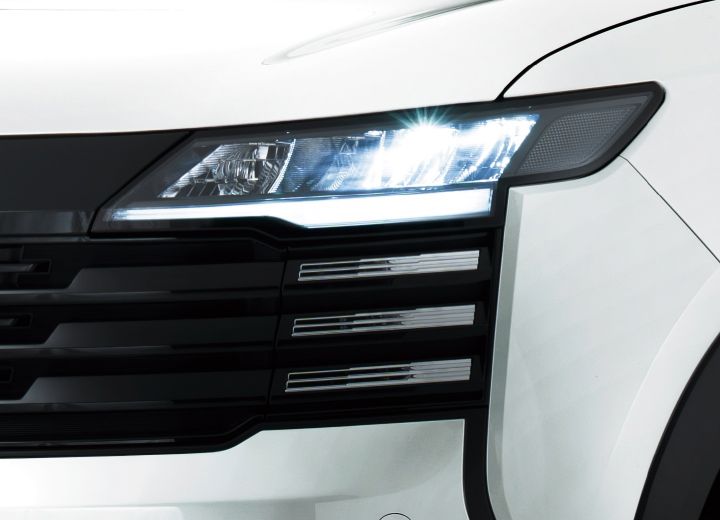 Close-up of the headlights and front grille of a white Nissan Kicks. The horizontal design lines and illuminated lights stand out.