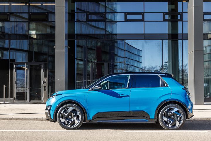 Im Sonnenscheint steht seitlich am Straßenrand ein leuchtend blauer Nissan Micra mit schwarzem Kontrastdach vor einem modernen Gebäude