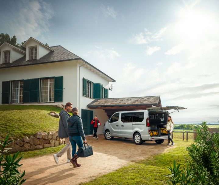 Nissan Primastar estacionada ao lado de casa, com casal a aproximar-se e criança atrás da viatura a carregar malas