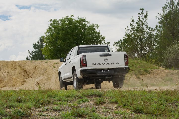 2026 Nissan Navara SL dual cab ute finished in Alpine White photographed from behind on a gravel clearing, displaying the rear bumper, tailgate lettering and dust trail.