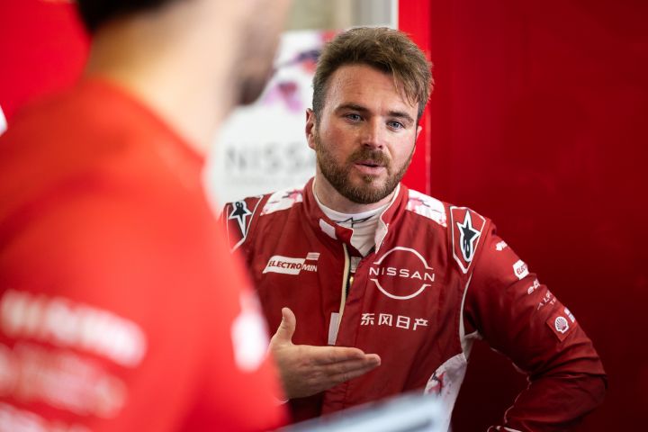 Oliver Rowland in seinem roten Rennanzug spricht mit seinen Ingenieuren in der Teamgarage.