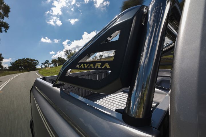 2026 Nissan Navara ST dual cab ute finished in Summit Silver showing a close view of the tray-mounted sports bar, ribbed tub floor and side rail details beside a rural road.