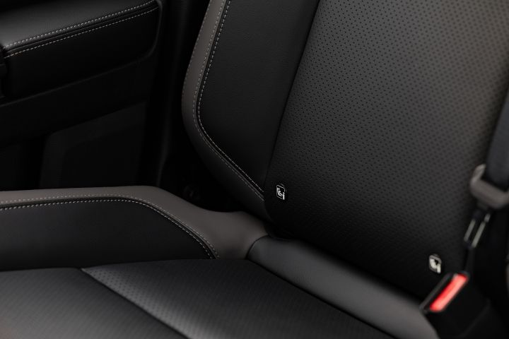 Close-up of a seat base and backrest in a 2026 Nissan Navara ST-X, showing perforated black upholstery, contrast stitching, and two small seat-anchor tags near the edge of the cushion.