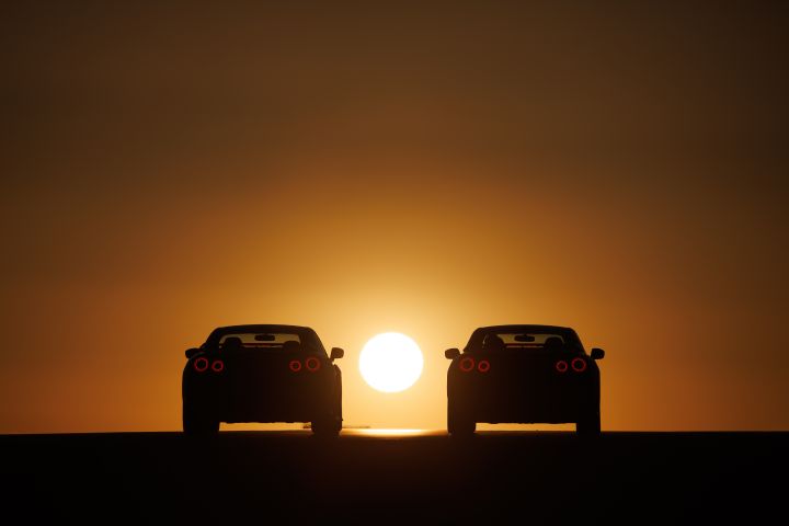Silhouette of two special edition Nissan GT‑R rear ends with a dark foreground and sunset in background