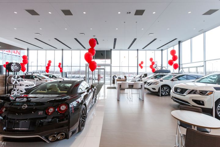 Salle d'exposition d'un concessionnaire automobile moderne avec une variété de voitures, dont une voiture de sport au premier plan, décorée de ballons rouges.