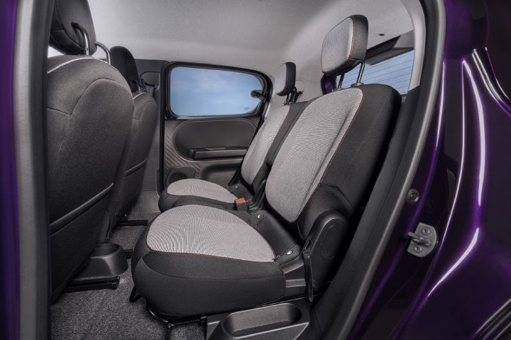 Photograph showing compact vehicle rear passenger compartment with two gray patterned fabric seats, black carpeting, door panels, and purple exterior frame. Open rear door, visible seat belts, adjustable headrests, window, and foldable seat structure highlight cabin layout and upholstery design.