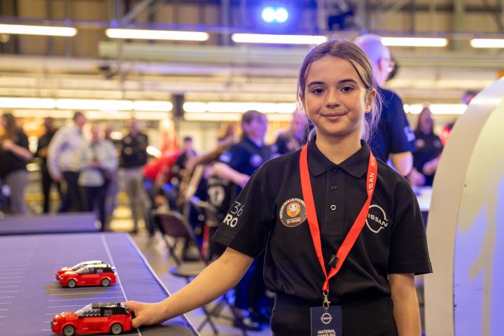 A school-aged child standing next to a small LEGO model of a Nissan Qashqai