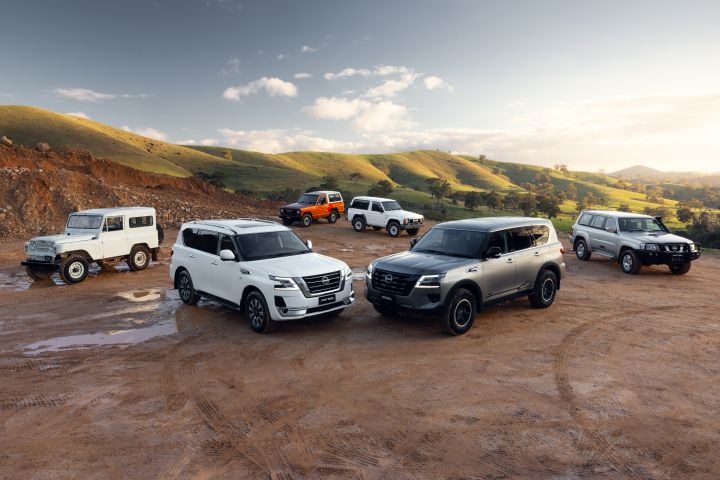 Nissan Patrol generations finished in various colours wide hero exterior lineup on muddy terrain with rolling green hills and soft evening light