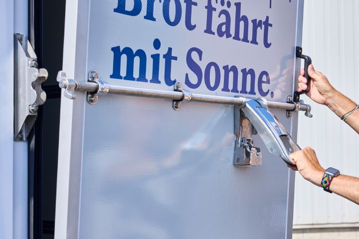 Zwei Hände öffnen die rechte Hecktür das Nissan Interstar-e mit Bäckereikoffer, diese lässt sich als Laderampe schräg bis zum Boden herabsenken