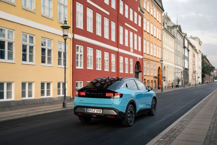 Blick von schräg hinten auf einen türkisen Nissan LEAF und das schwarz abgesetzte Rückfenster, das Auto fährt an typisch dänischen Stadthäusern in Kopenhagen vorbei