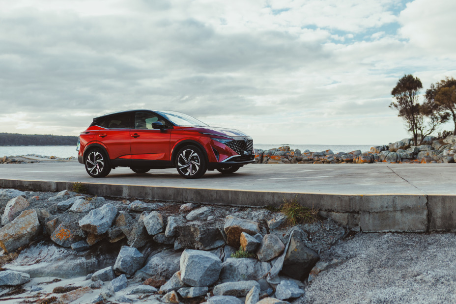 A red Nissan Qashqai is parked by the sea