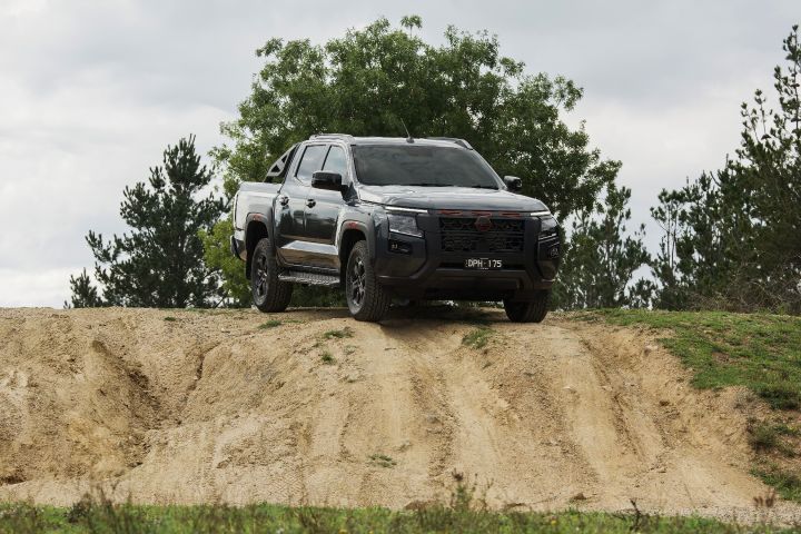 2026 Nissan Navara PRO-4X finished in Boulder Grey positioned in a front-three-quarter crest shot on a sand ridge above steep erosion lines and low green brush.