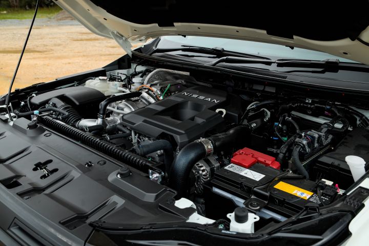 2026 Nissan Navara SL dual cab ute finished in Alpine White with the bonnet open, revealing the engine bay layout, Nissan engine cover, battery placement and intake hardware